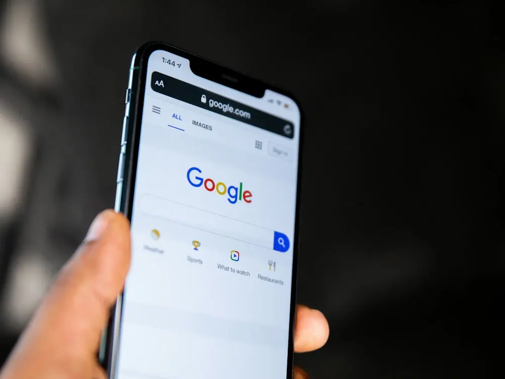 A hand holding a phone showing the Google search page