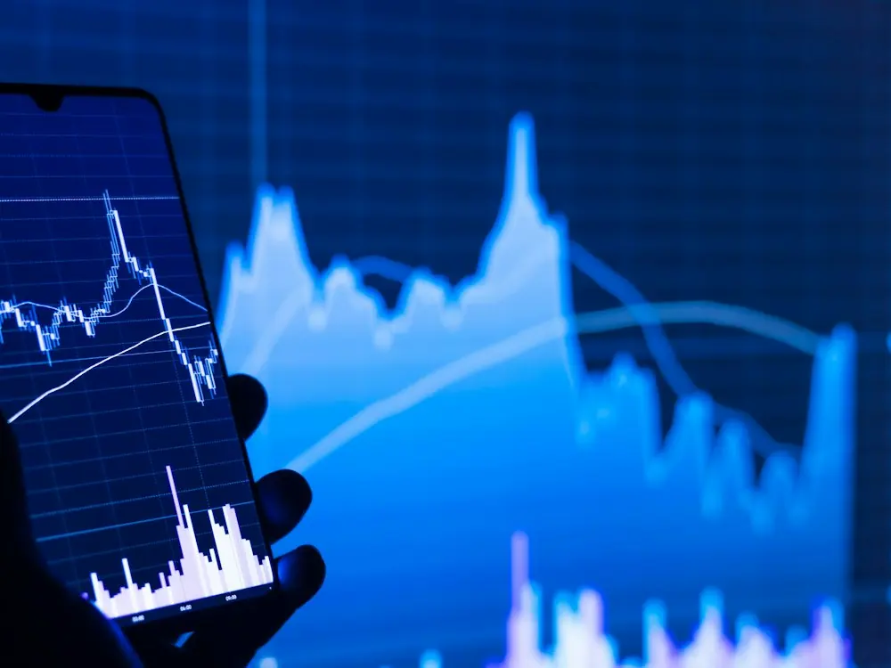A phone showing a stock market chart in front of a bigger chart